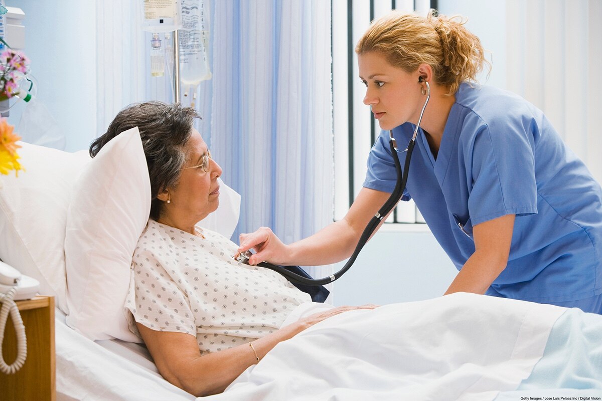The nurse examines an older adult client positioned with their head elevated in a hospital bed.