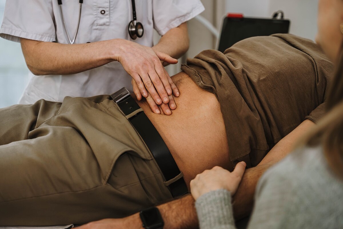 A nurse palpates the stomach of a client visiting a gastroenterologist.